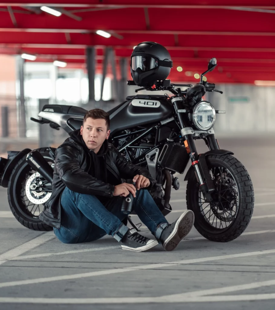 Junger Mann sitzt neben seinem geparkten Motorrad in einem Parkhaus. Er hält dabei eine Bluewater Flasche in der Hand