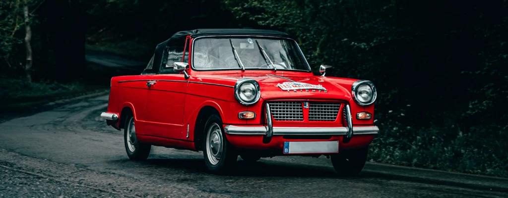 Kaiser Classic Imagefoto. Darauf zu sehen ein roter Oldtimer auf einer Waldstraße