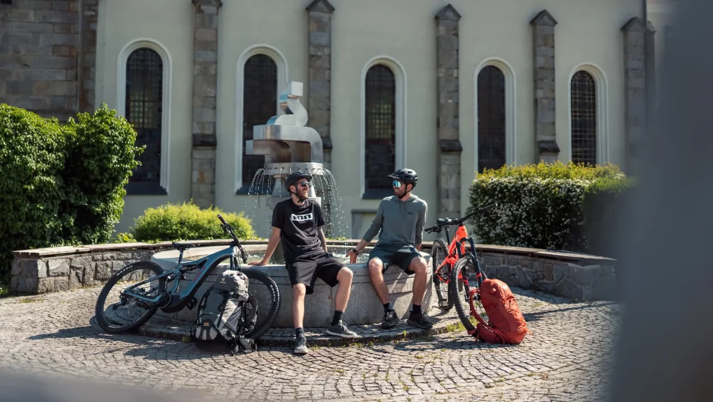 2 Mountainbiker machen eine Pause am Brunnen während der Mountainbike Tour