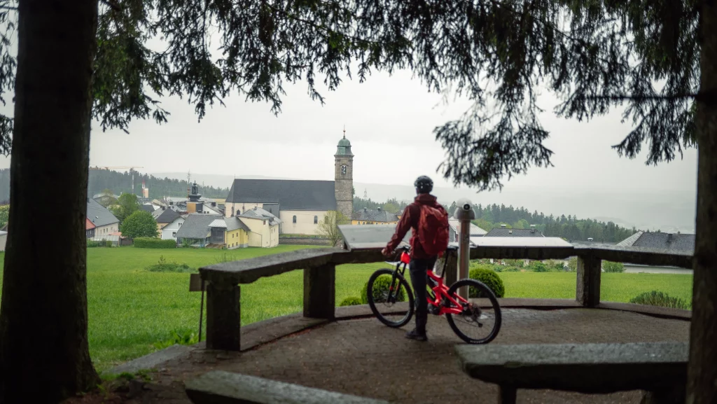 Biker steht am Waldrand vor dem Bike, mit dem Blick auf ein verregnetes Pfarrkirchen